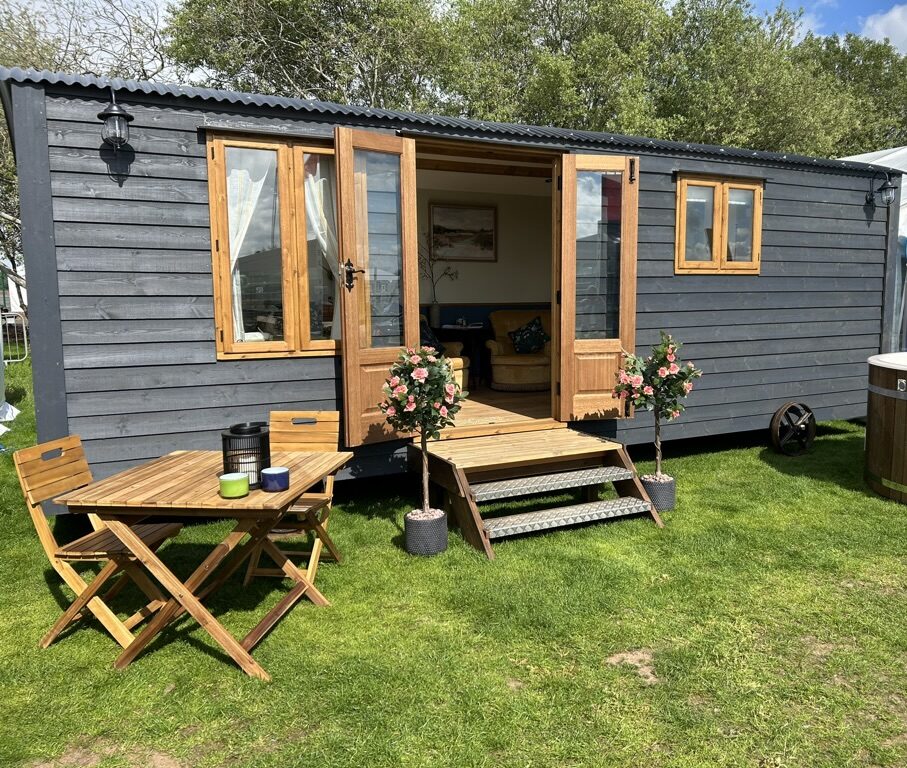 Black shepherd's hut outside on grass with table and chairs