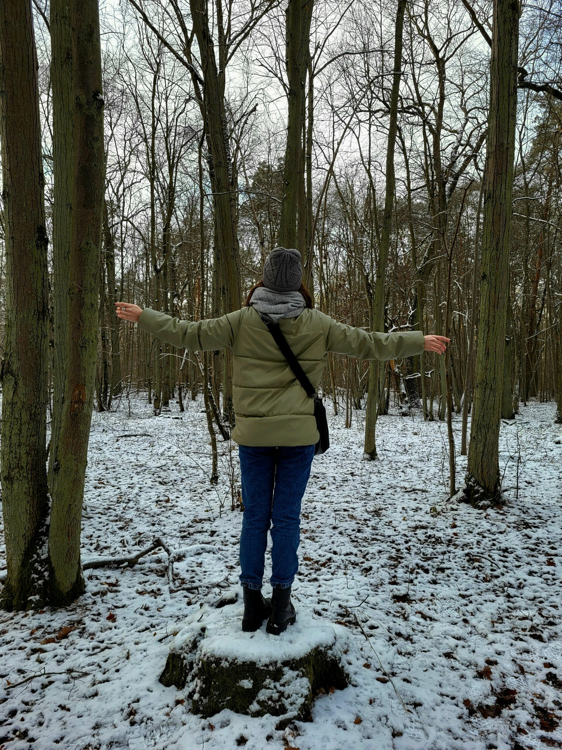 Woman standing on tree stump in snowy woodland